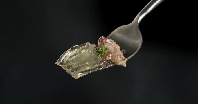 Aspic jellied meat on fork, close-up footage on dark background.