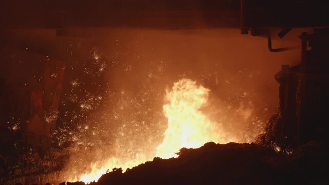 Molten iron ore pouring from industrial furnace creating sparks