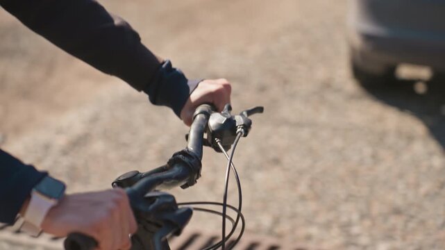 white cyclist hands on handlebars closeup showing grip, brake control and watch on wrist while navigating gravel path near suburban lawn focused technique, tactile detail and outdoor motion