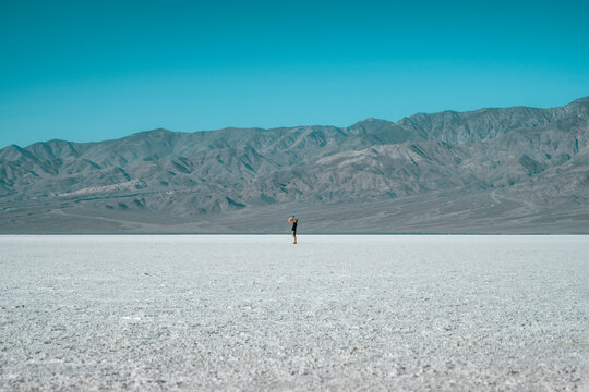 A breathtaking panoramic view of Death Valley, with a father and his baby standing on a vast, flat desert plain, appearing tiny against the immense landscape.