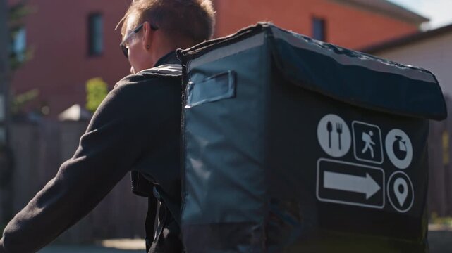 white delivery cyclist with insulated backpack pedaling along sunlit residential street, focused expression, thermal bag with icons, closeup perspective, morning light and soft shadows, last mile