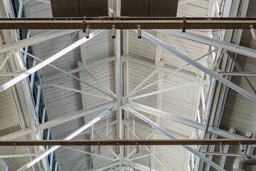 Spacious industrial interior with metal beams, corrugated metal ceiling and walls, fluorescent lights, textured floor possibly concrete, expansive, no people or text Candid photograph style, taken