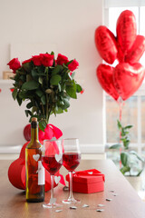 Glasses of wine, gift boxes and bouquet of roses on wooden table in kitchen, closeup. Valentine's...