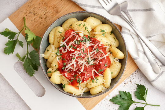 Bowl of tasty gnocchi with tomato sauce and cheese on white background