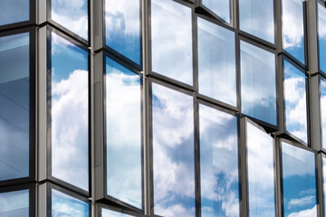 Modern corporate office skyscraper architecture facade with glass windows pattern reflecting blue sky clouds on building exterior background