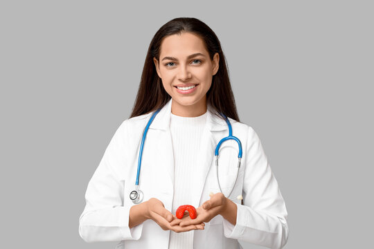 Portrait of female doctor with thyroid model on grey background