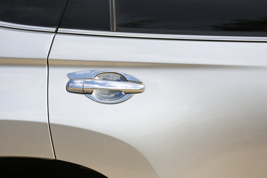 Close up shot showing detail of modern silver automobile door handle on side of luxury car with shiny white metallic paint and dark tinted glass window for privacy travel and transport concept