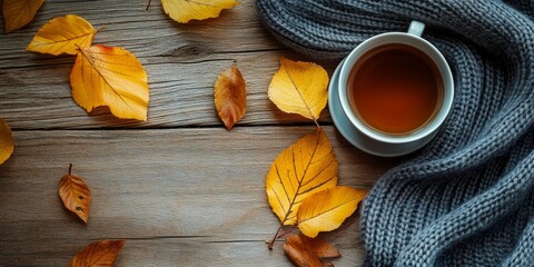 A warm cup of tea surrounded by vibrant autumn leaves on a rustic wooden surface, topped with a cozy gray scarf.