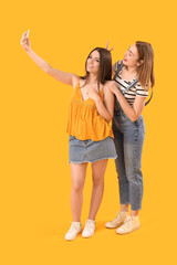 Fototapeta premium Female friends with mobile phone taking selfie on yellow background