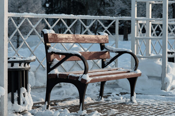 A wooden bench sits in a snow-covered park, adorned with a generous layer of fresh snowfall. The...