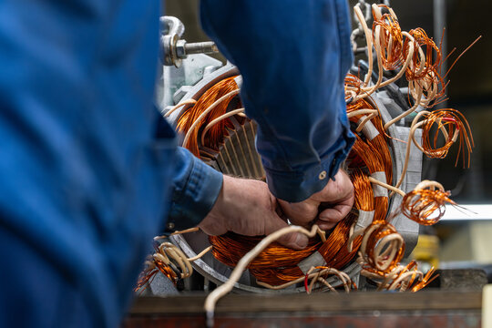 Gros plan sur un technicien en atelier industriel manipulant des bobinages en cuivre lors de la r&eacute;paration ou de l&rsquo;assemblage d&rsquo;un moteur &eacute;lectrique.
