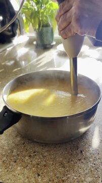 Batiendo con batidora de brazo el&eacute;ctrica un pur&eacute; de crema de calabaza en cazuela en encimera de cocina