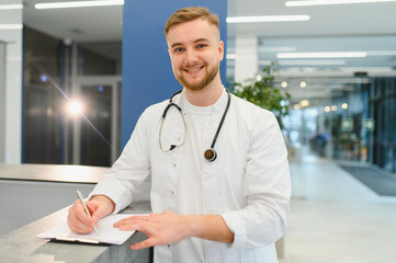 Smiling young doctor writing medical report in clinic