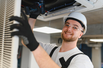 Technician repairing ceiling air conditioning unit with drill