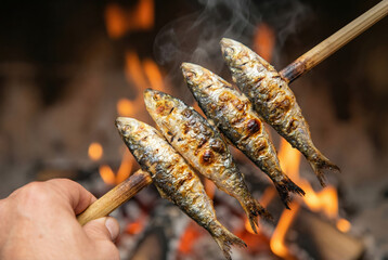 Varios espetos de sardinas asadas acompañadas de limones en un gran plato blanco sobre una mesa de madera rústica © Iombi