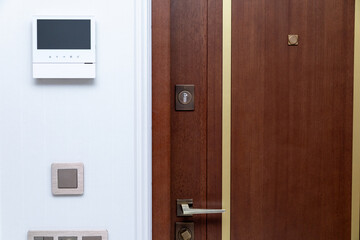 Obraz premium Modern wooden entrance door with gold fittings, peephole, intercom system on white wall and electrical switches, shows contemporary home design with functional elements for security and communication