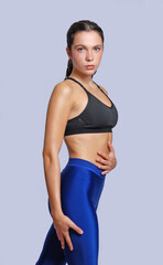 Young fitness athletic woman wearing blue legging and black top posing touching her abdomen with determination and discipline expression stand on white background.