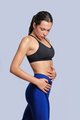 Young fitness athletic woman wearing blue legging and black top posing touching her abdomen with determination and discipline expression stand on white background.