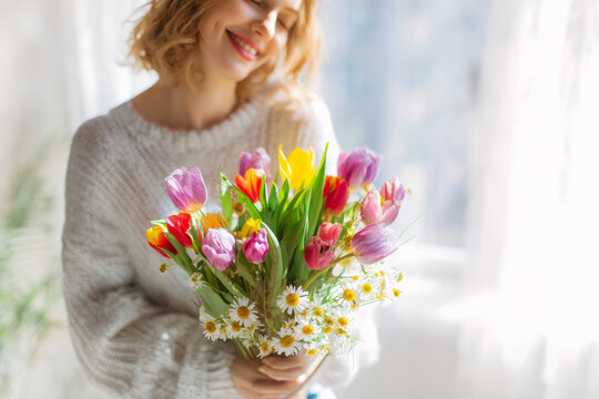 Woman holding bouquet of tulips and daisies in bright indoor space, soft sunlight, joyful expression, springtime International Women's Day concept for stock photography