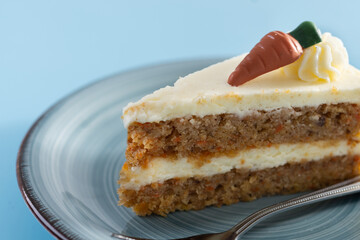 Carrot cake slice with cream cheese frosting on blue background