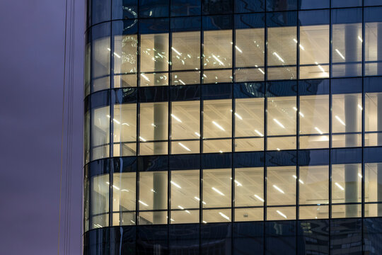 Modern corporate building glass office facade with bright windows at night lights creating urban architecture pattern and business skyline mood