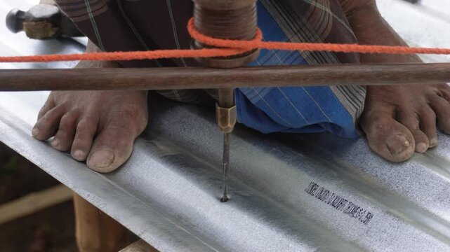 person using a traditional hand drill to create a hole in a corrugated metal sheet