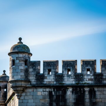 Dramatic view of ancient stone battlements and crenellations on a fortress wall structure against a bright blue sky, symbolizing defense and history, outdoor, protective, construction
