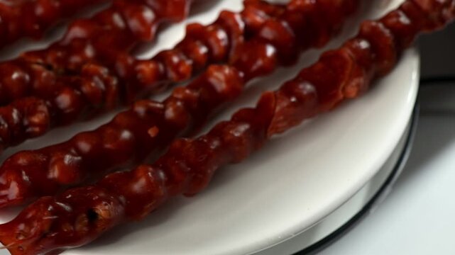 A traditional Georgian churchkhela sausage, packed with hazelnuts, rotates slowly. Highlights its glossy, textured coat and nutty interior. A unique sweet.