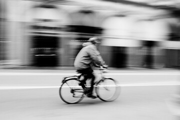 man riding a bicycle in motion captured with motion blur on a city street. The black and white photo emphasizes speed, urban life and environmental consciousness. Street photography. © Davide Zanin