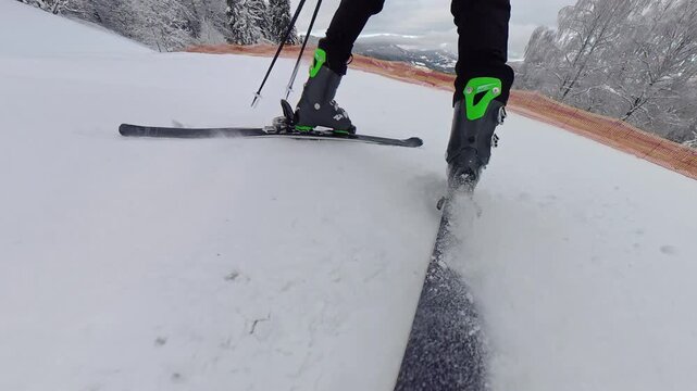 Close up view of professional ski boots and skis carving through snow, action winter sport photography on mountain slope with white powder spray