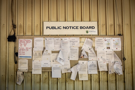 Adamstown, Pitcairn Islands - 02 January 2026: View of a public notice board plastered with various announcements against a corrugated metal backdrop.
