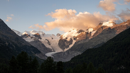 Obraz premium A breathtaking morning view captures the beauty of Piz Bernina, showcasing its glaciers and rugged peaks in the Swiss Alps, bathed in warm sunlight against soft clouds.