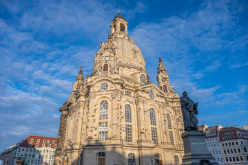 Fototapeta premium The Frauenkirche stands tall in Dresden under a blue sky. Visitors explore the area, and the church is a central point during the Christmas season for locals and tourists.