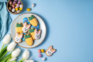 Obraz premium Easter spring holiday background with easter cookies in a plate: bunny, carrot and egg with white tulips