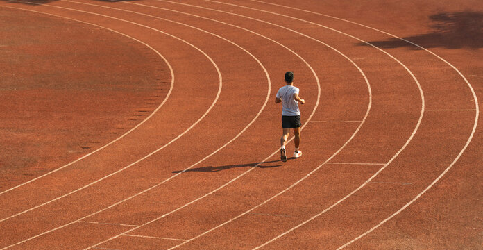 Rear view of a runner in sportswear training on a red running track Athletic man sprinting
