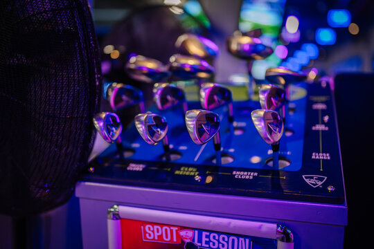 Golf clubs displayed on a rack at Topgolf venue in Dubai, illuminated by colorful lights and modern decor