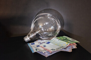 Light bulb and stack of euro banknotes. Electricity consumption, energy costs, and finance. Electricity sale and cost, payment.