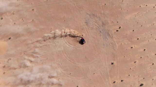 Top down FPV drone shot capturing an off road buggy drifting in sand. Circular tire marks and dust clouds form graphic patterns highlighting speed motion control and raw off road energy.