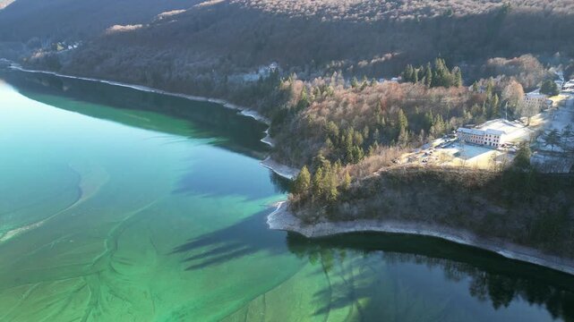 Aerial drone footage of Barcis Lake, Italy: sunny winter day, turquoise water and mountains, with snow-capped peaks visible in the distance. Ideal for travel, nature and scenic stock footage.