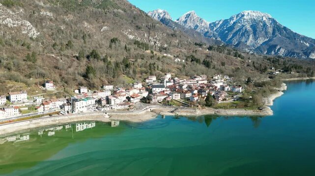 Aerial drone footage of Barcis Lake, Italy: sunny winter day, turquoise water and mountains, with snow-capped peaks visible in the distance. Ideal for travel, nature and scenic stock footage.