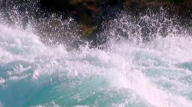 Vibrant turquoise waters churn and crash as they rush over Huka Falls. Splashes of water fly into the air, creating a dazzling display of nature's power during the daytime in New Zealand.