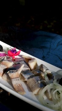 Pieces of herring fillet are sprinkled with green onions on a white plate. Salted sea fish, a traditional cold appetizer. Close-up, top view. High quality 4k footage