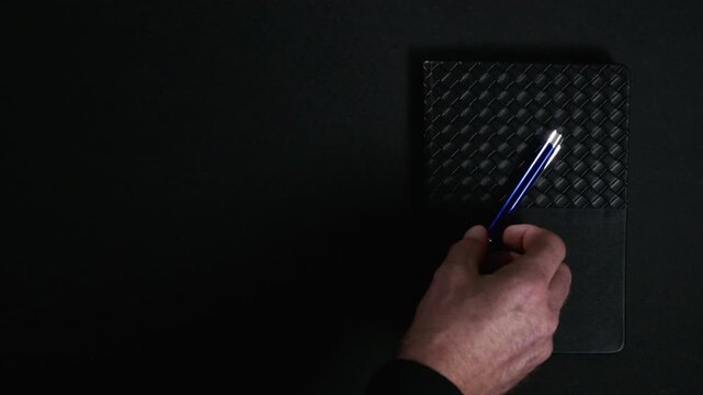 Hand placing pen on notebook on dark background