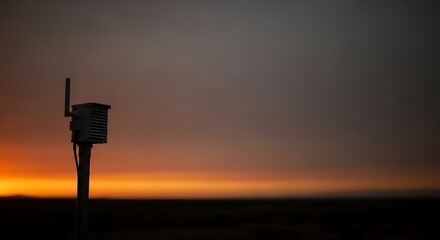 A silhouette of an outdoor environmental sensor monitoring air quality with a smoke detector, set against a wildfire smoke filled sunset background. Perfect for environmental reports,