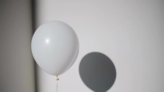 A white balloon floats against a white and gray background, its shadow cast on the right