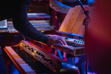 Pianist hands playing keyboard on stage during live concert with neon lights