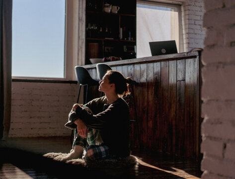 Dreamy woman sitting on floor at home in cozy sweater, rural lifestyle