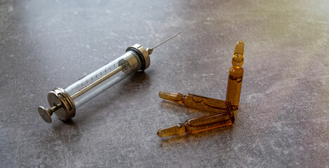 A glass medical syringe and glass ampoules are on the table.Vintage medicine.Reusable syringe.