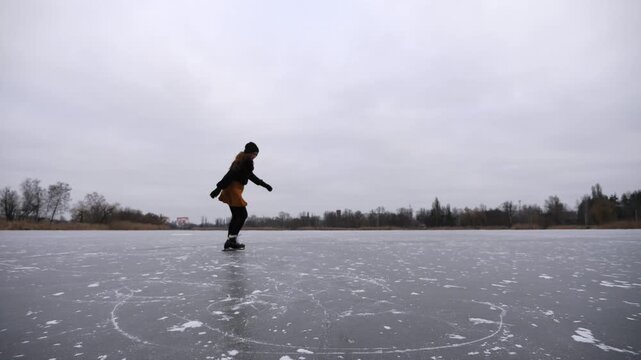 Young sportswoman shod in figure skates sliding on ice river at winter. Female skater practicing skills at lake on frozen day. Girl enjoying sport and having active leisure at cold weather. Slow mo