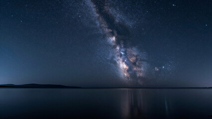 Breathtaking Milky Way galaxy arches across the dark night sky, brilliantly reflected on serene lake waters, revealing the vast beauty of the cosmos